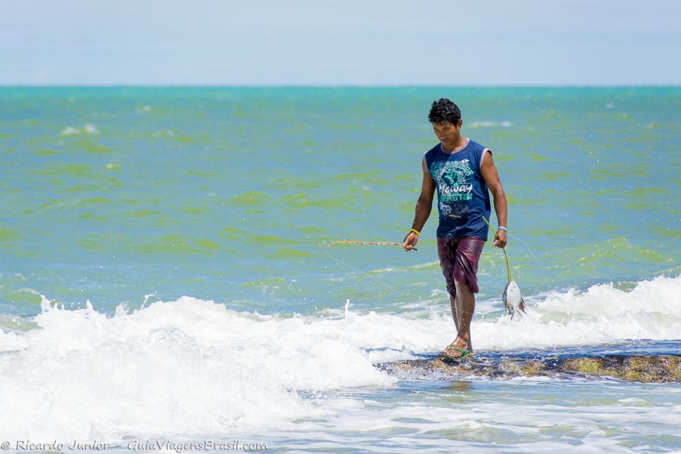 Imagem de pescador com peixe no mar da Praia de Caraiva.